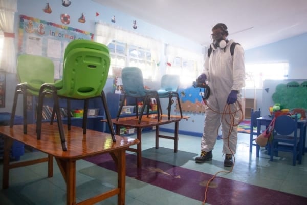 Suited man disinfects classroom. Deep cleaning service Cambridge anticovid-19