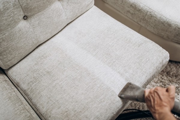 Male worker removing dirt from light sofa with professional vacuum cleaner indoors, closeup/ Upholstery Cleaning service in Cambrigde